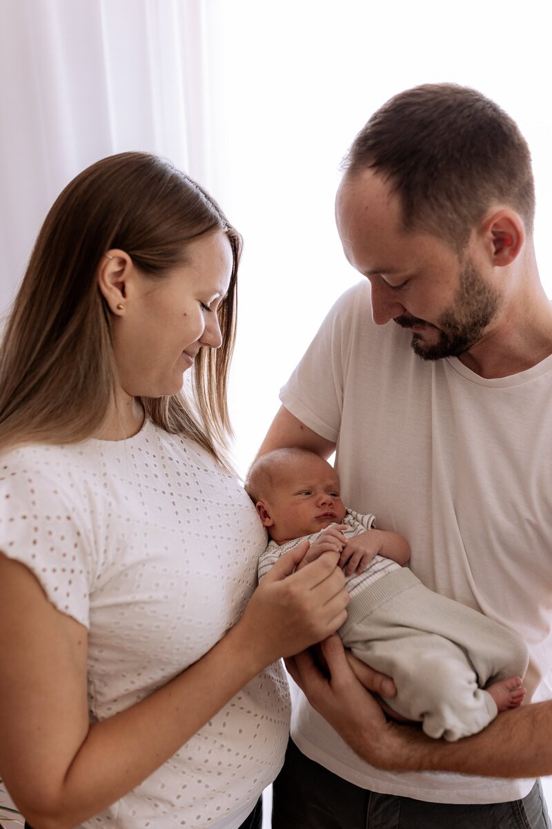 Vater haelt Baby im Arm und Mutter haelt die Hand des Babys