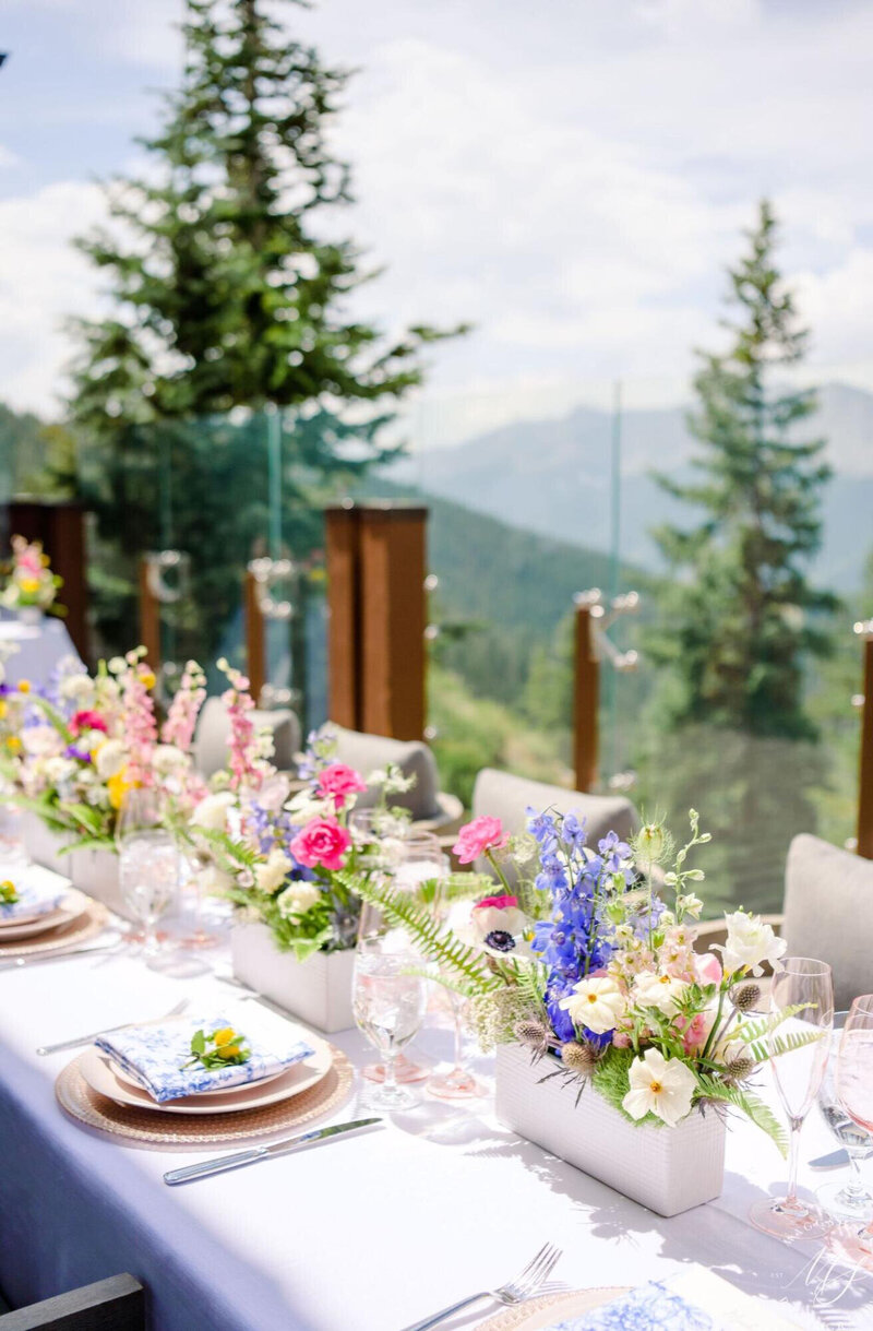 A colorful tablescape with flowers and table settings at The Little Nell in Aspen with a view of trees and mountain peaks