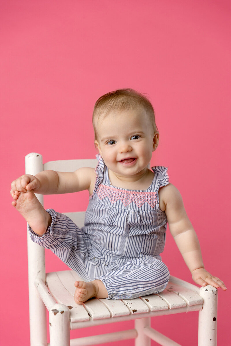 Photo of a baby girl holding her toes and smiling on a pink background