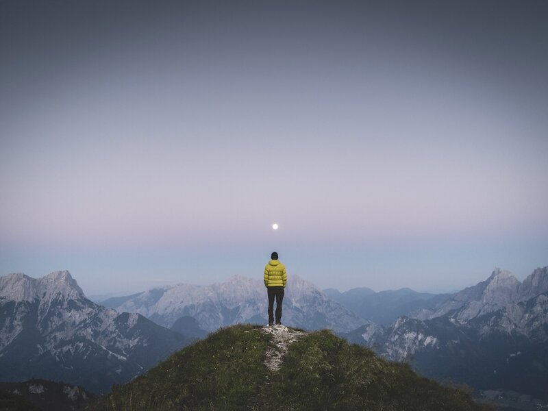 Solo man looking out at a breathtaking mountain range at high altitude, embracing the perfect workation setting for remote workers at The Campus Alps.com, offering inspiring views and a peaceful environment for focused productivity in the Alps.