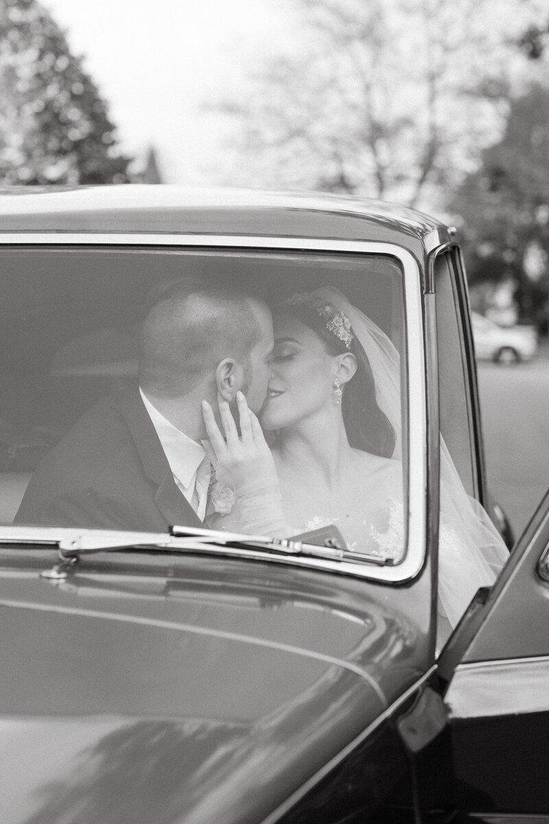 bride and groom sitting inside a vintage car about to kiss each other