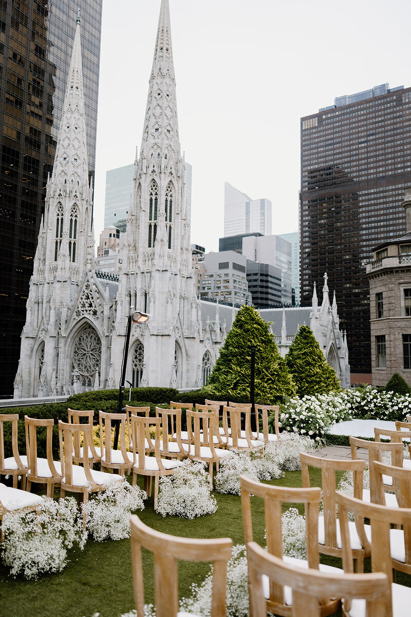 Outdoor ceremony setup beside a cathedral with white flowers.