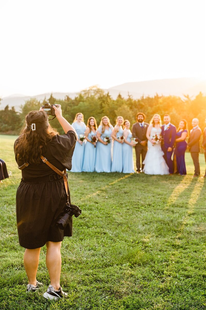Virginia wedding photographer in all black dress, boots, and coat holding her camera and walking across a white studio space and looking to the side