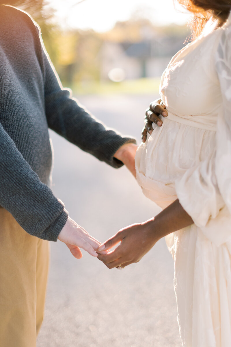 Husband holds hands with his wife and mother-to-be at maternity portrait session