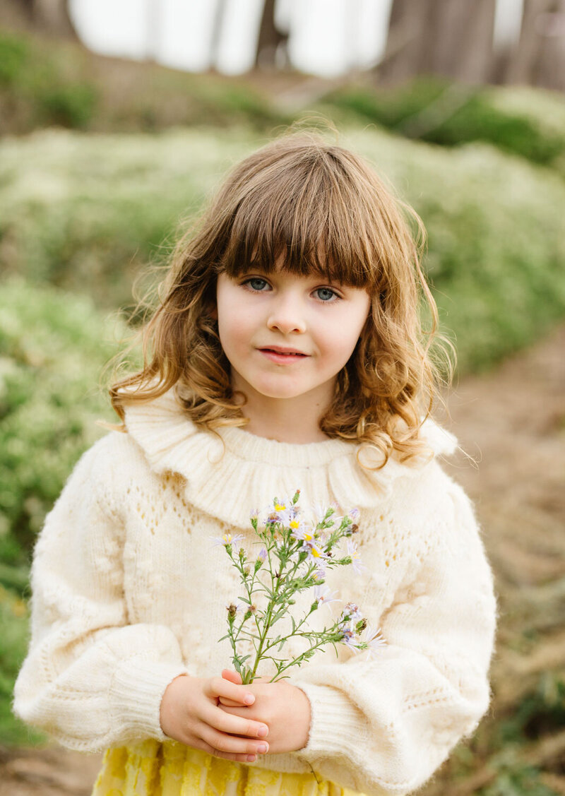 Girl Child holding a plant smiling softly, Bay Area woods
