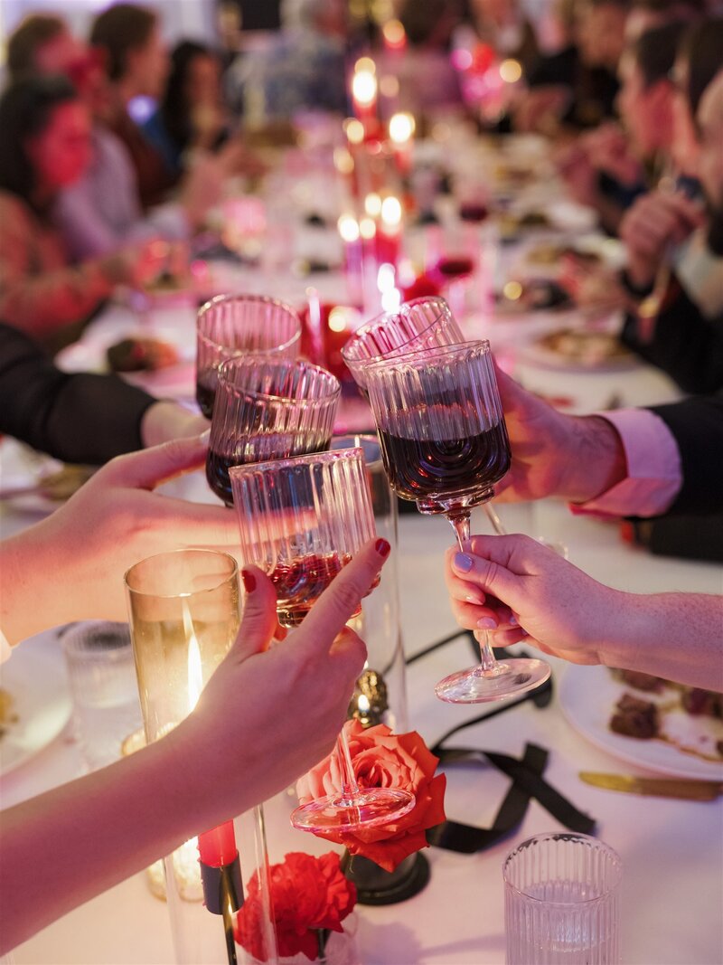 wedding reception dinner table with guests holding beverages in hands clinking in cheers