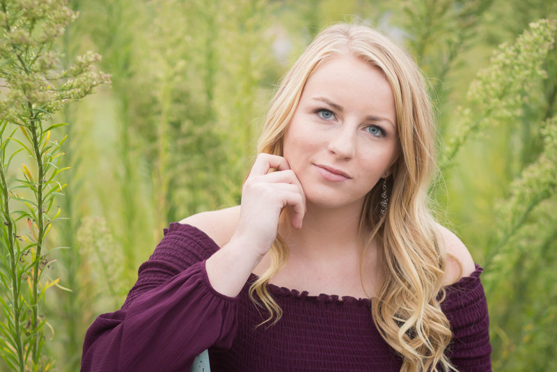 triway high school senior girl standing in tall dead grasses in fall with colorful scarf with grey shirt, far left hand in holding scarf senitriway senior girl sitting in tall green grasses with yellow tops, wearing burgandy off the shoulder dress sitting in chair looking at camera and not smiling, photographed at a park  in wooster ohio  photographed by jamie lynette photography canton senior photographer