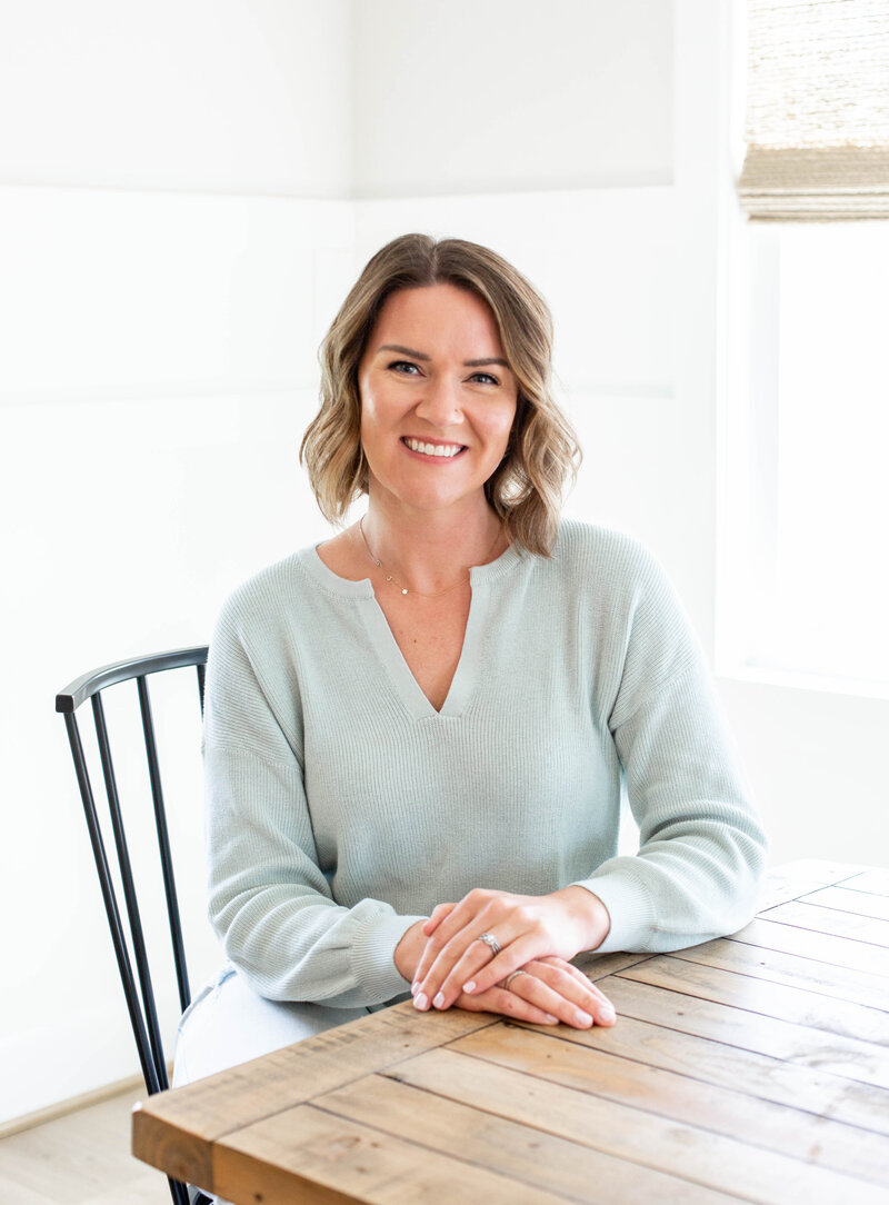 Headshot of Sarah, a lactation consultant from Richmond, wearing a light teal sweater sitting at a wooden table
