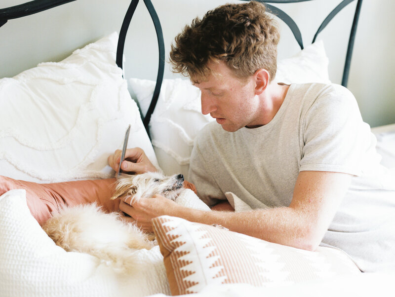 The groom grooms his puppy on a bed in a cabin on Paint Rock Farm in preparation for the wedding ceremony.