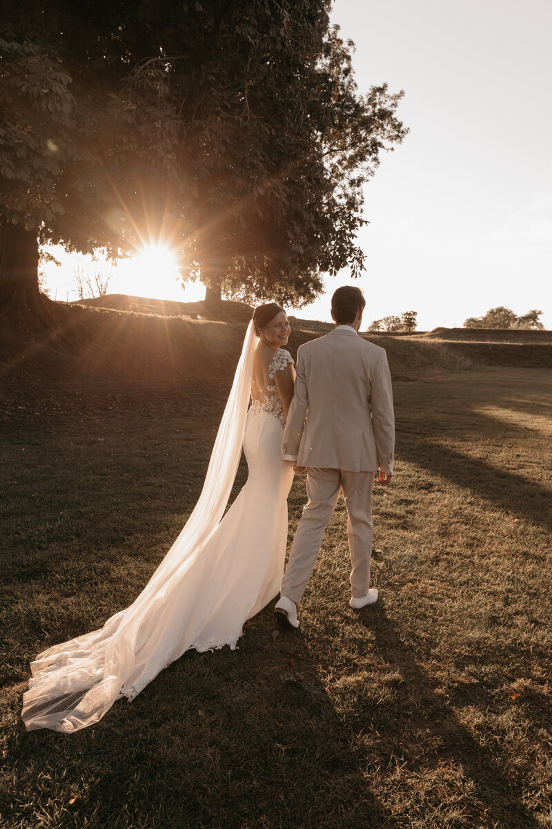 Bruid en bruidegom lopen hand in hand tijdens zonsondergang. 