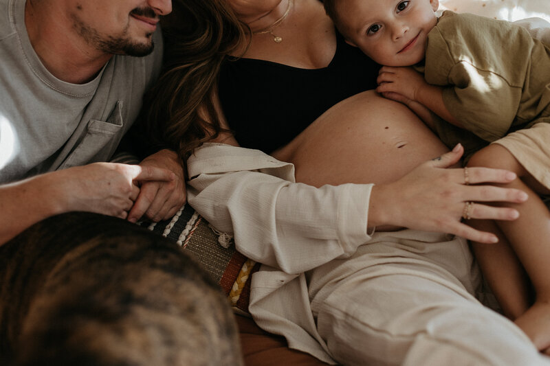 Close-up of a pregnant woman’s belly, with her partner and child lovingly touching it.