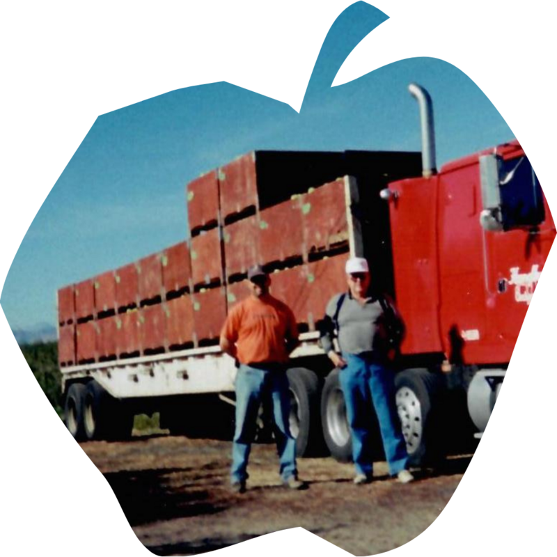 Two men standing next to a semi truck full of apple bins in the middle of an apple orchard in the Wenatchee Valley.