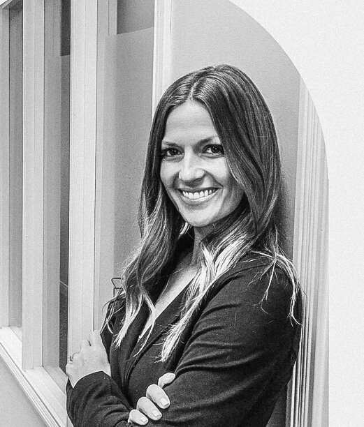 Jennifer Lindsey, ultrasound business coach, leaning on a wall with windows