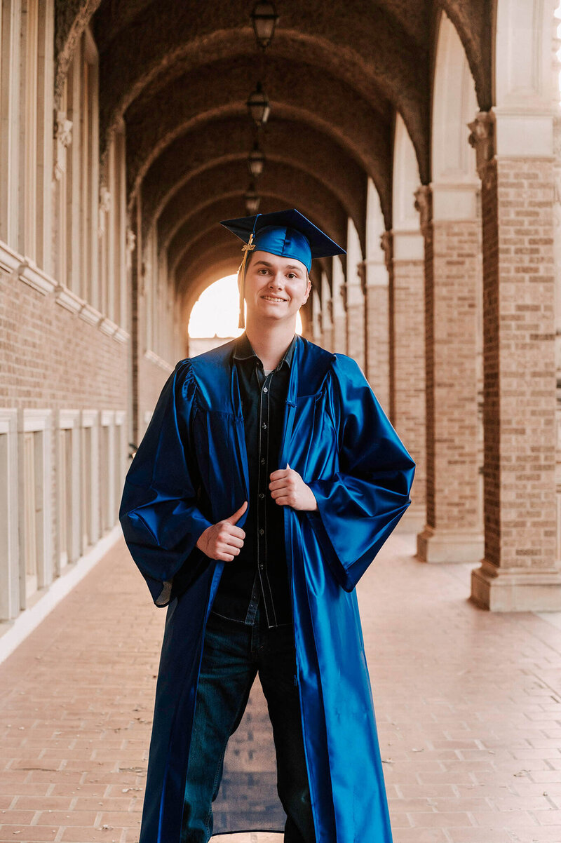 High school graduate in his cap and gown standing in an outside brick hallway