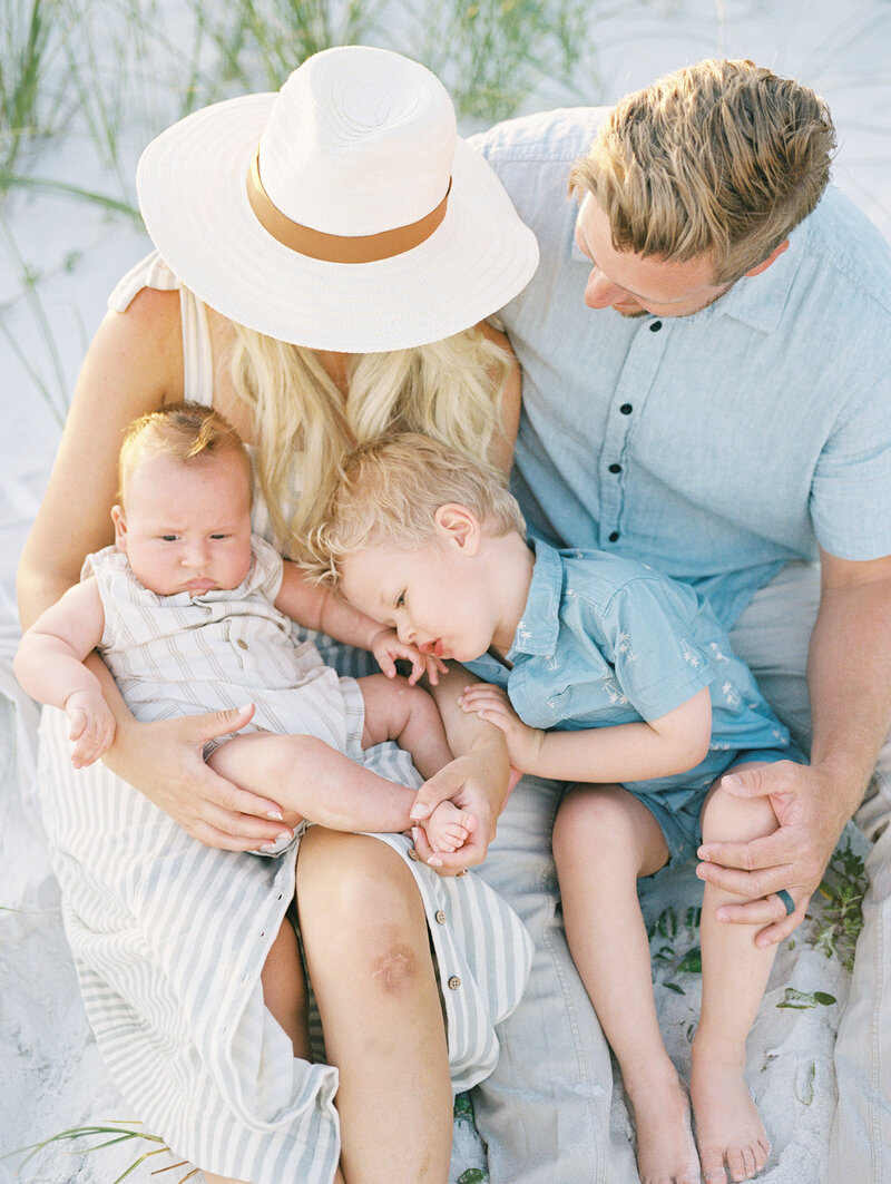 Mom and dad holding their two children in their laps while sitting on the beach