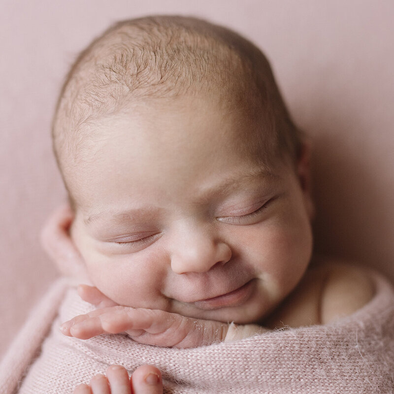 Close-up of baby face smiling, newborn, swaddled in baby pink, Perth in home newborn session