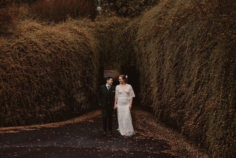 A wedding couple standing in front of a plan covered bridge holding hands