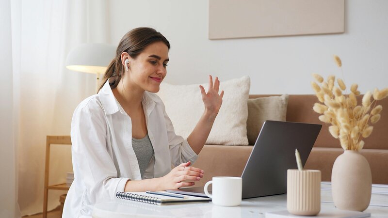 Individual waving at a laptop screen during online group voice and performance lesson. 