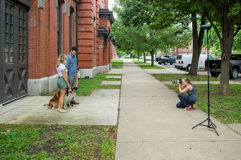 Jen Stitt capturing a joyful moment with an engaged couple and their dog during a summer engagement session in Philadelphia, highlighting their connection and the vibrant cityscape.
