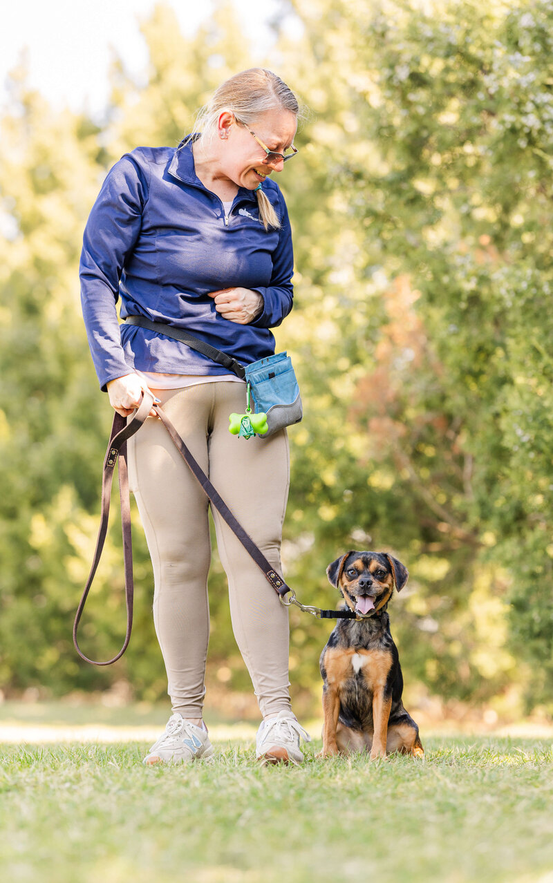 Female Dogology University trainer smiling at a dog who is also smiling at the camera during a board and train session at a local park