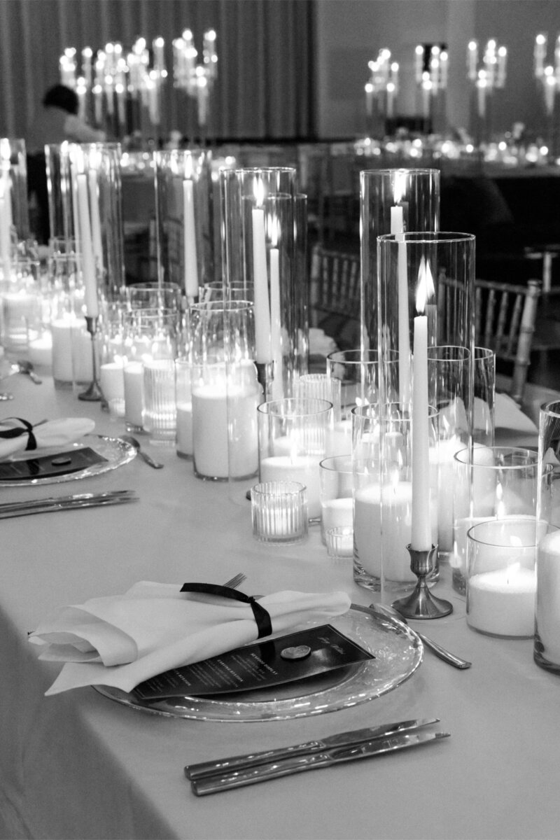 A formal dining table with candles in glass holders, elegant place setting, and a white tablecloth.