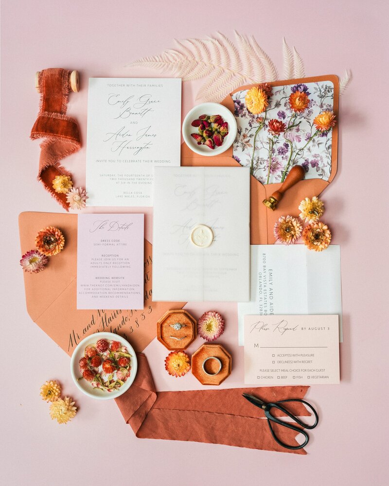 Bright pink flatlay of wedding invitations with fresh fruit and florals.