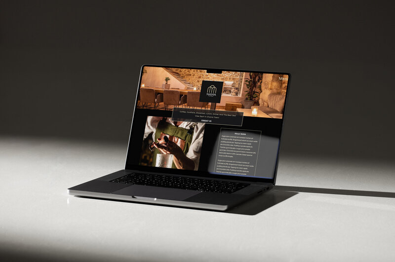 A laptop displaying a website for "NAMA," a bar offering coffee, cocktails, breakfast, lunch, dinner, and a scenic view in Town. The site features images of a cosy interior and a bartender preparing a drink, highlighting an inviting atmosphere for guests.