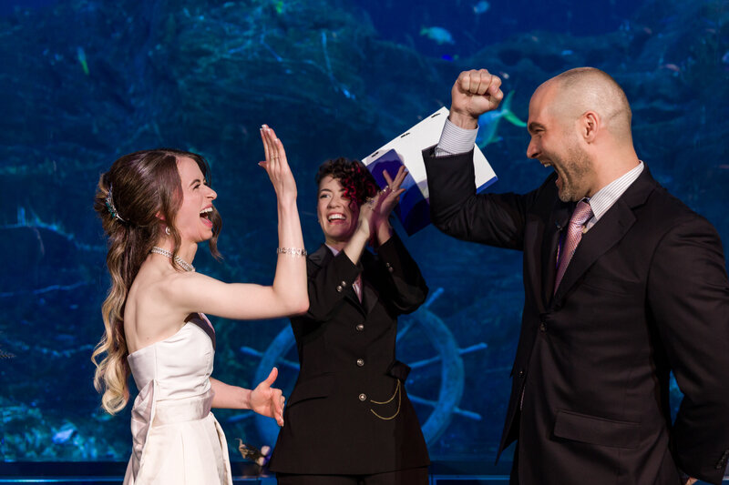 Playful wedding moment as a couple high-fives during their ceremony in the Ocean Realm Theater at Adventure Aquarium.