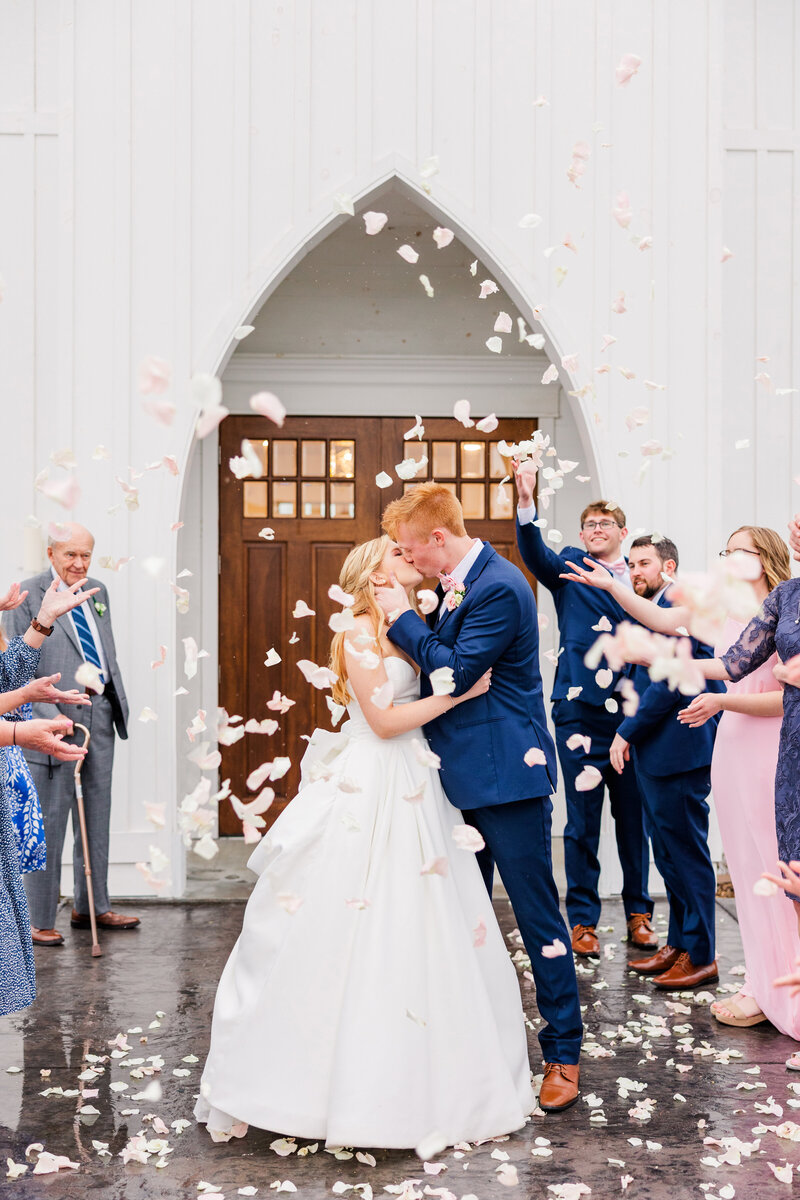 bride and groom kissing as guests throw confetti