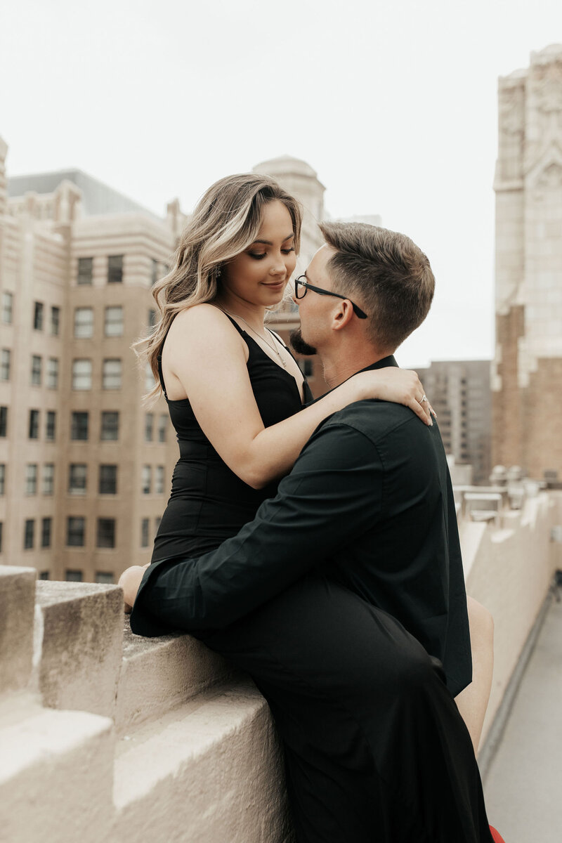 Woman sitting on ledge in front of tulsa skyline holding and looking at  man