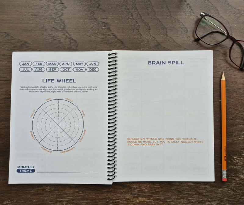 The Life Wheel and Brain Spill pages of the Time Magic Planner open on a wooden surface, with a pair of glasses and a pencil placed nearby.