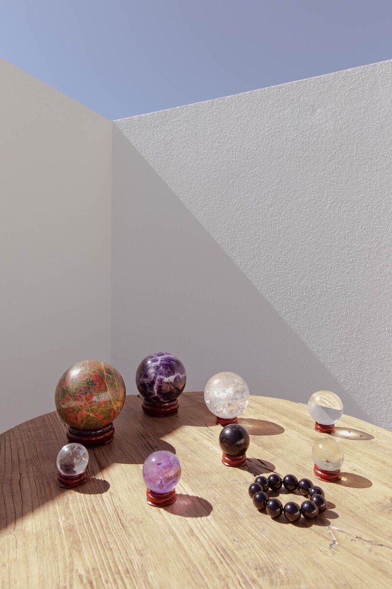 A selection of various sized crystal balls of different nature, displayed on a rustic table  by a white concrete wall, looking beautiful.