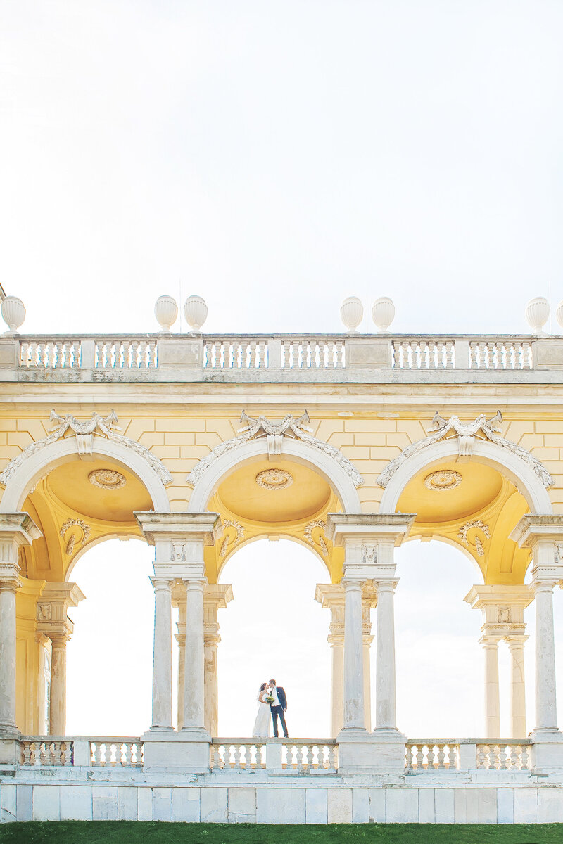 Bride and groom kissing under marble archways