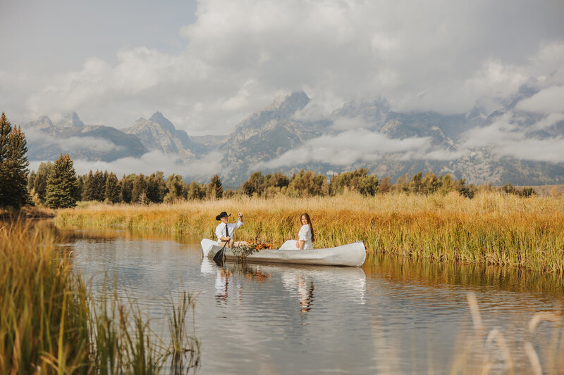 Bride and groom rowing a canoe down a quiet river in Glacier National Park, surrounded by nature.