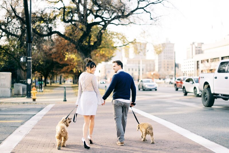 A man and woman walking two dogs on a loose leash while crossing a busy city crosswalk