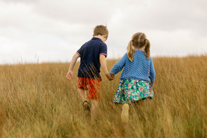 A brother and sister walking holding hands in long grass on Haworth moor