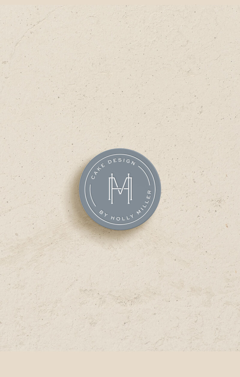 Blue-grey brand submark for Cake Design by Holly Miller on textured stone background