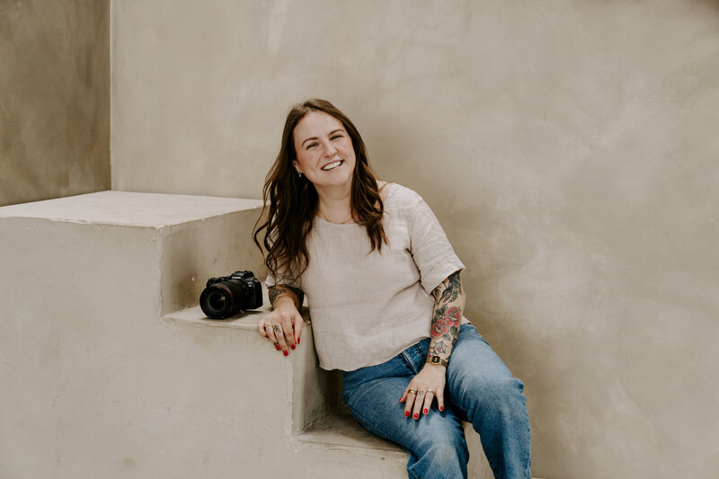 Katelyn sits on the ground against a black wall, looking to the right.