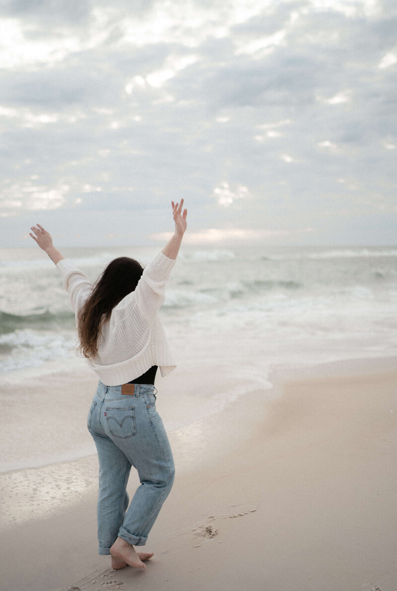 photographer Brittney Stanley holds up arms towards sky, wearing levis & white sweater in PCB florida