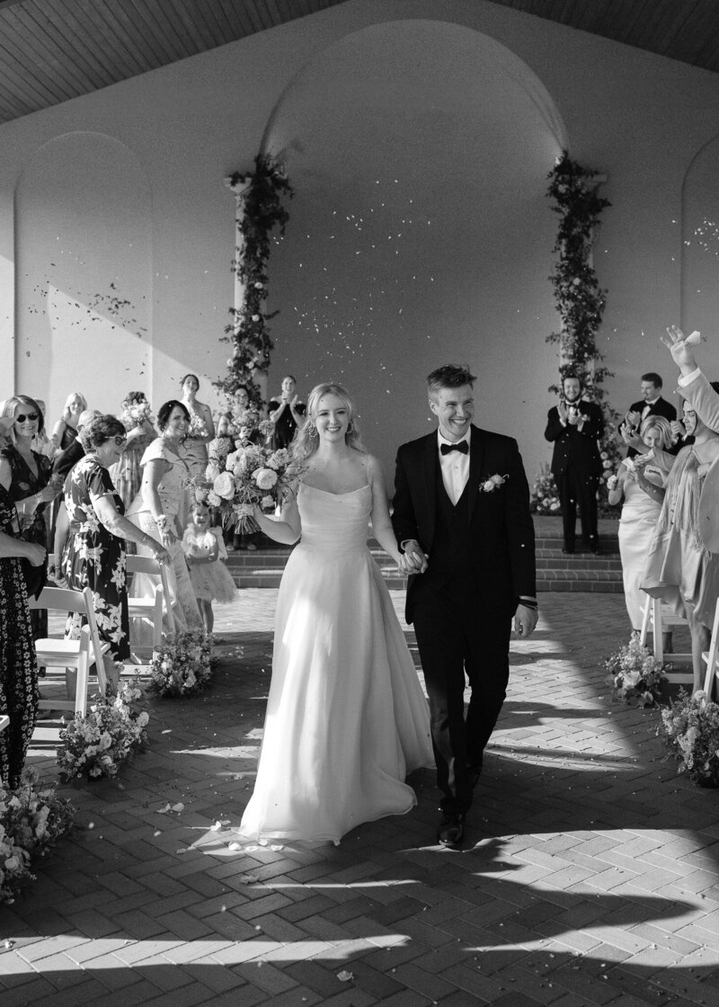 A couple walks down the aisle as their friends and family shower them with flower petals