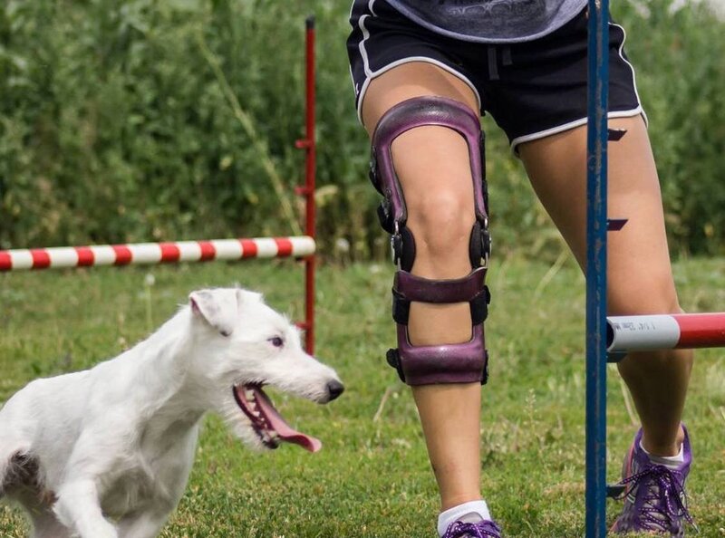 A woman, supported by a custom knee brace, running alongside her furry companion.