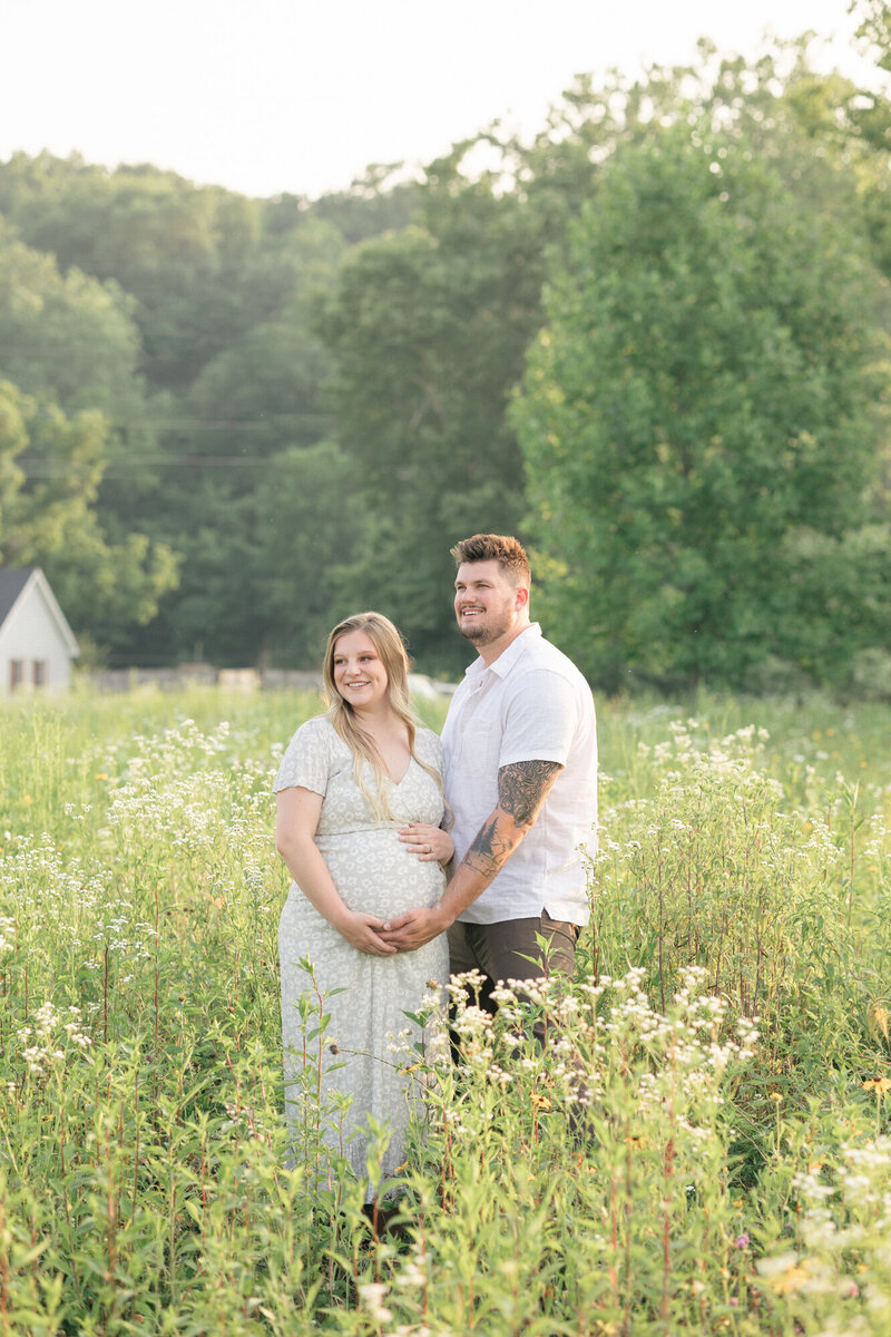 Expecting parents embracing moms growing bump in a field of wildflowers during their maternity photos