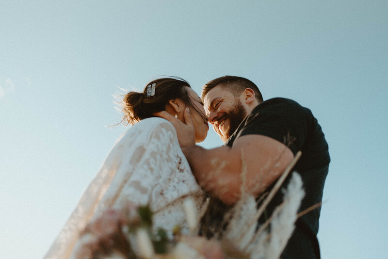 bride and groom kissing against blue sky