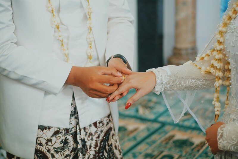 Close-up of a traditional Indonesian wedding ring exchange, with the groom placing a ring on the bride’s hand, captured by Chi Ramos Photography.