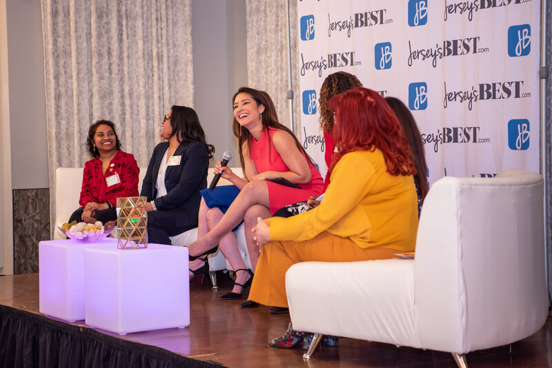 A group of women panelist on the stage talking and laughing at an International Women's Day Business Summit.