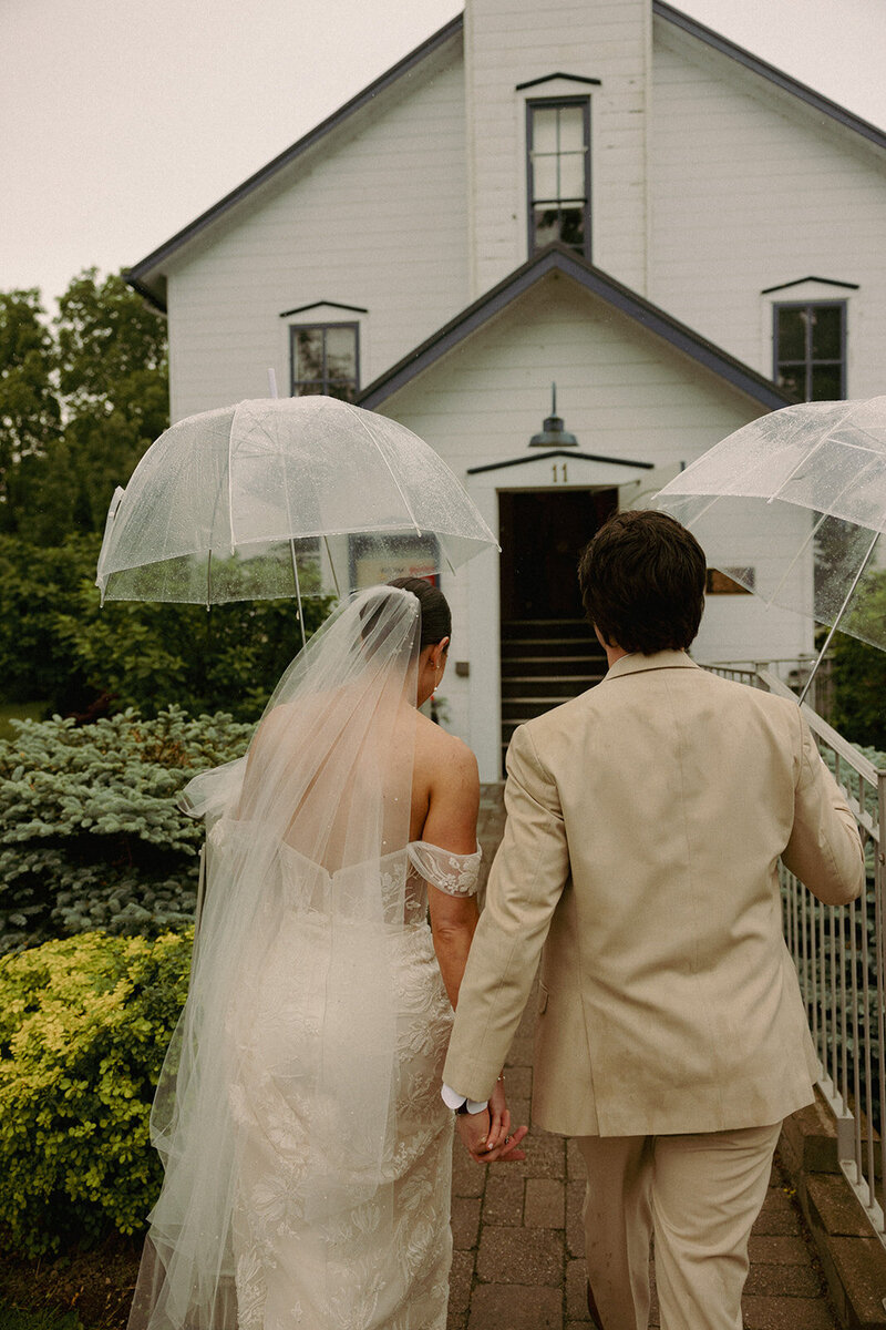 bride and groom walking in the village of Bayfield with umbrellas on their wedding day