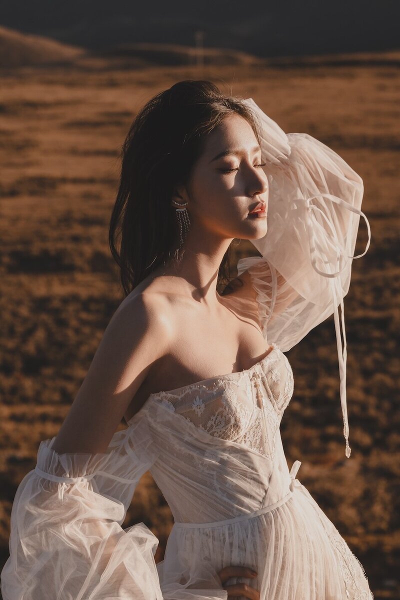 A bride photographed in the golden evening light in a wild field with. mountains in the background.