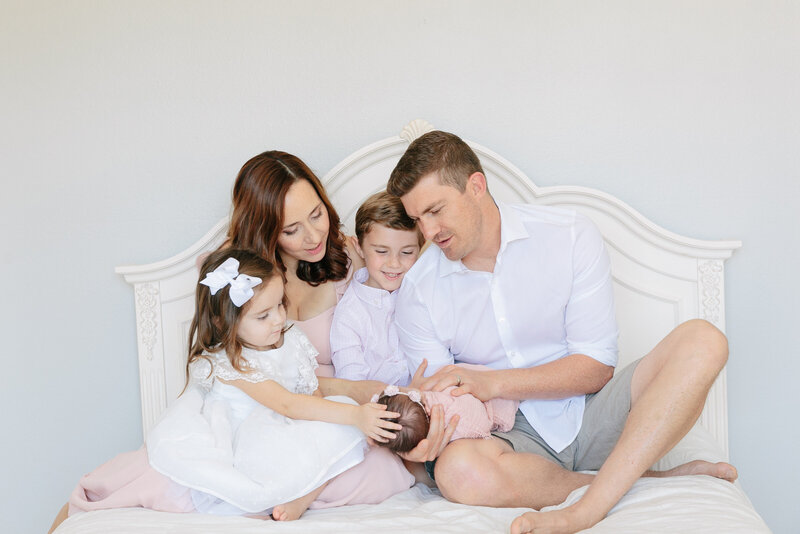 A family sitting on a bed together smiling at a newborn baby