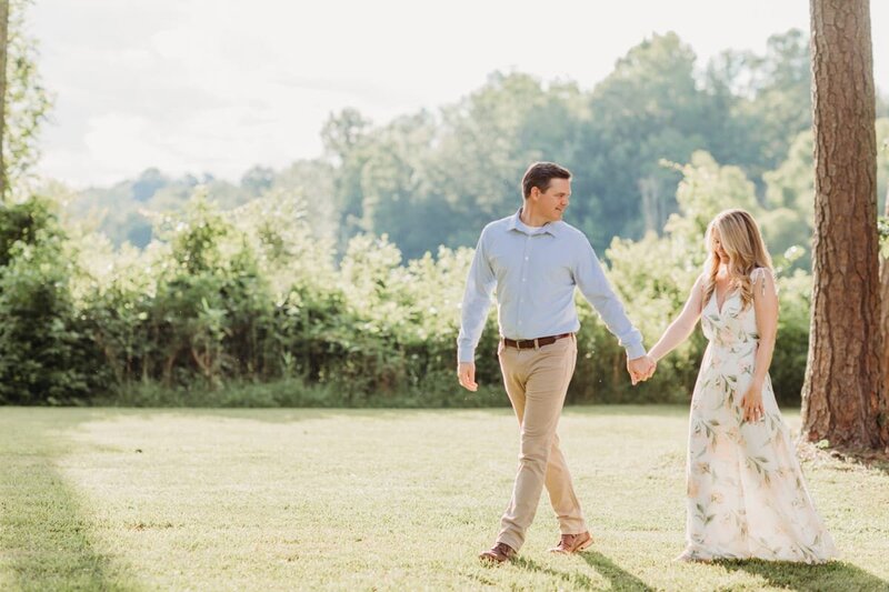 Engagement session photo of man leading his future bride across a grassy lawn.