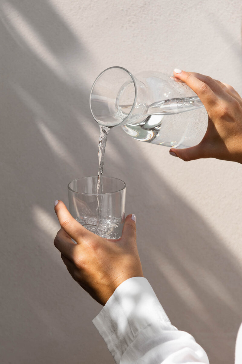 Photo of a woman pouring clean drinking water into a glass showing a wellness habit of staying hydrated